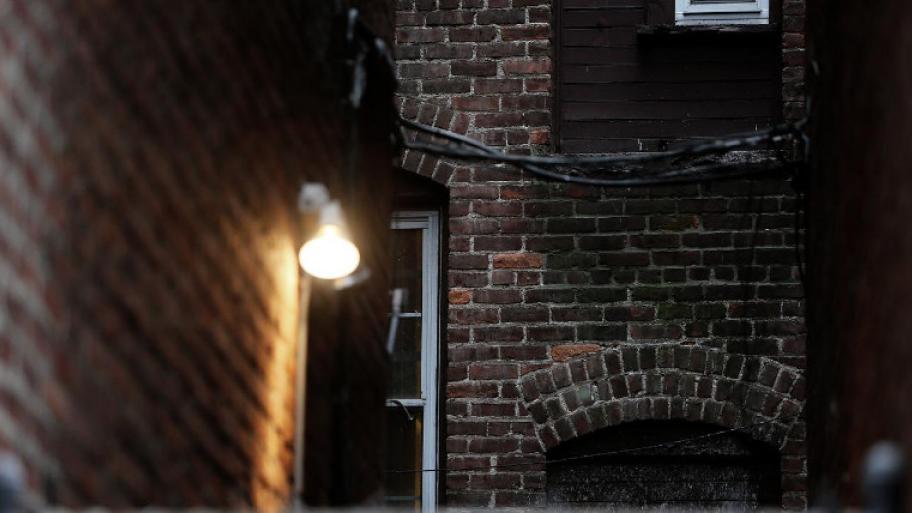 Gemäuer eines Backsteinhauses, an der Wand hänge eine Lampe, die Licht an die Mauer wirft