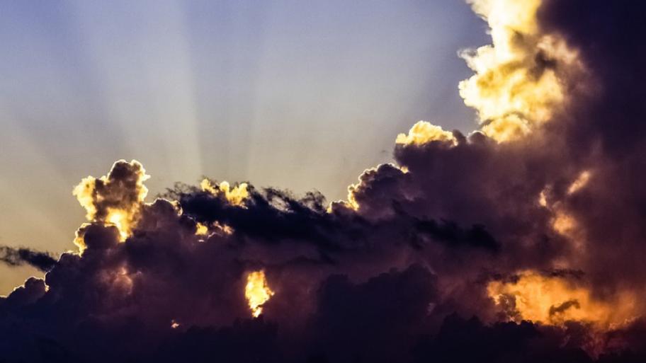 ein Himmel ist zu erkennen. Hinter einer großen, graublauen Wole ist ein wenig Sonne zu erkennen