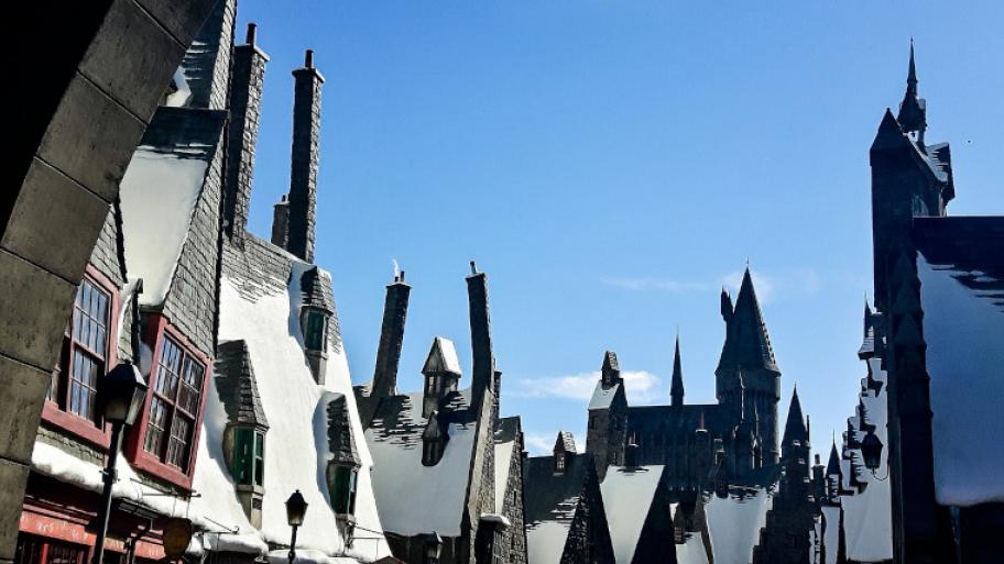 Hausdächer mit Schornsteinen und Dachgauben, in der Mitte am Horizont die Dächer eines Schlosses (Hogwarts)
