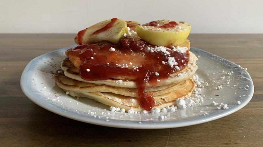 auf einem weißen Teller mehrere frisch gebackene Pancakes, garniert mit Birnenstückchen und roter Beerenmarmelade