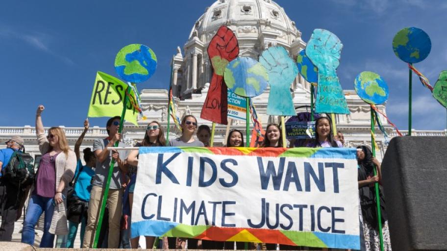 eine Gruppe von Jugendlichen demonstriert vor einem historischen Gebäude in den USA für Klimagerechtigkeit, auf ihrem Transparent steht "Kids want climate justice"