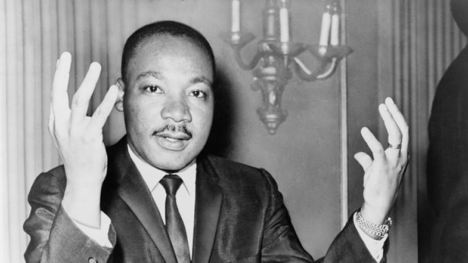schwarz-weiß Porträt von Martin Luther King, er hält beide Hände hoch und trägt einen dunklen Anzug
