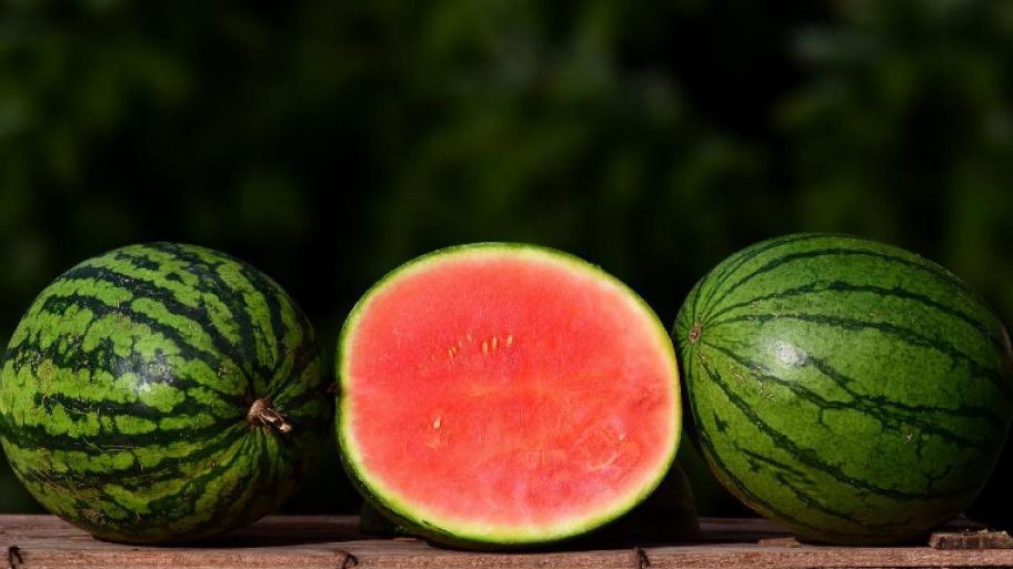 Drei Wassermelonen liegen nebeneinander, die Melone in der Mitte ist zur Hälfte aufgeschnitten, die Melonen links und rechts sind ganz