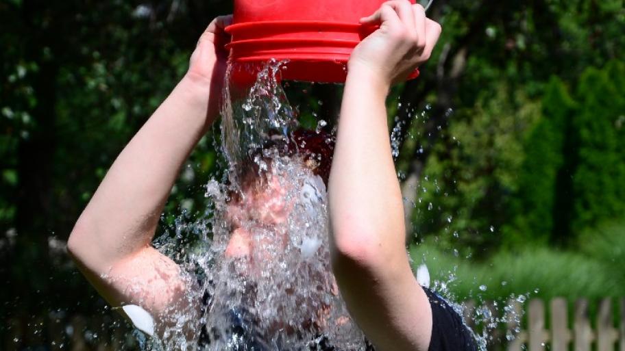 EinTeilnehmer der ALS Ice Bucket Challenge kippt sich mit einem roten Eimer Eiswasser über den Kopf