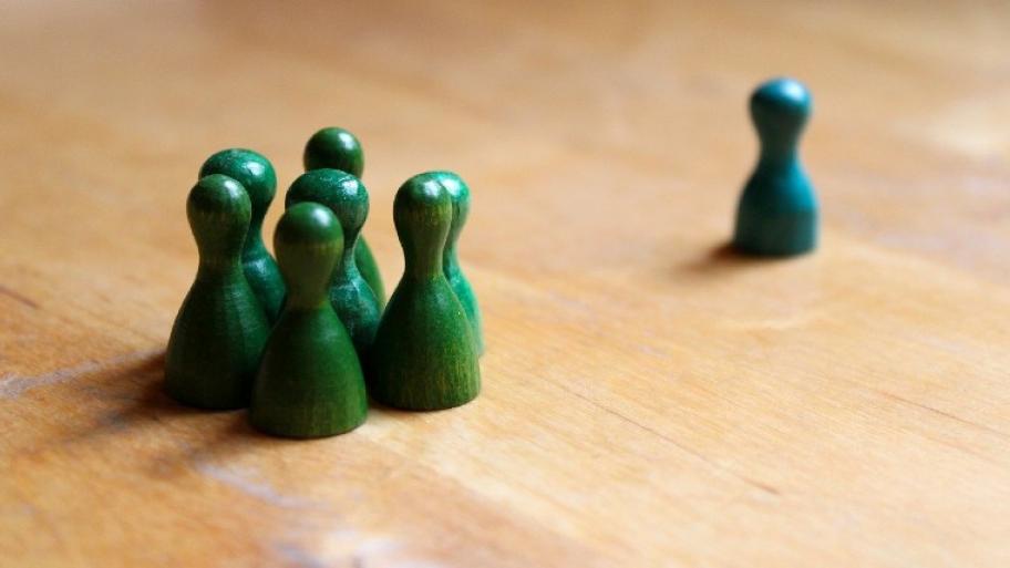 Grüne Spielfiguren stehen in einer Gruppe, eine blaue Spielfigur wird von der Gruppe ausgeschlossen