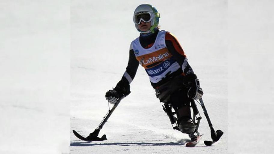 Eine Para-Sportlerin mit Helm auf der Skipiste. Sie hat ein Monoski und zwei Unterstützung zwei Skistöcke mit Kufen. 