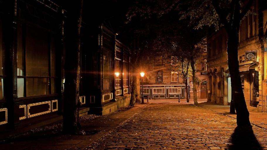 Straße mit Häusern an der Seite. Es ist sehr dunkel, man sieht die Straßenlaternen, von denen das einzige Licht kommt.