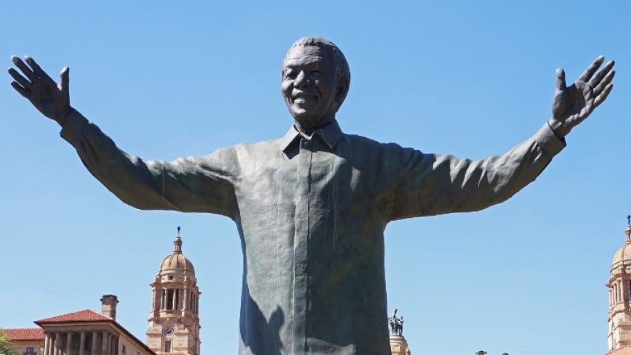 Ausschnitt der bronzenen Nelson Mandela Statue in Pretoria, Südafrika, zu sehen ist Oberkörper und Kopf der Statue, Mandela hat die Arme ausgebreitet und lächelt, im Hintergrund blauer Himmel