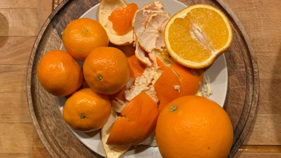 Orangenschale, aufgeschnittene Orange, Mandarinen und Orangen liegen auf einem Teller auf einem Holzbrett