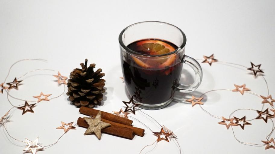 Punsch in Glastasse mit Orangenscheibe garniert, Tannenzapfen und Zimtstangen links neben der Tasse, Sternengirlande als Deko 