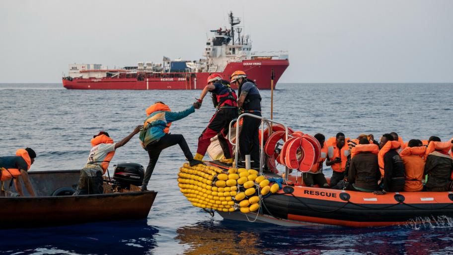 2 Boote auf dem Meer, die Menschen im linken Boot haben alle Rettungswesten an, ein Mensch hilft einem anderen ins andere Boot zu steigen