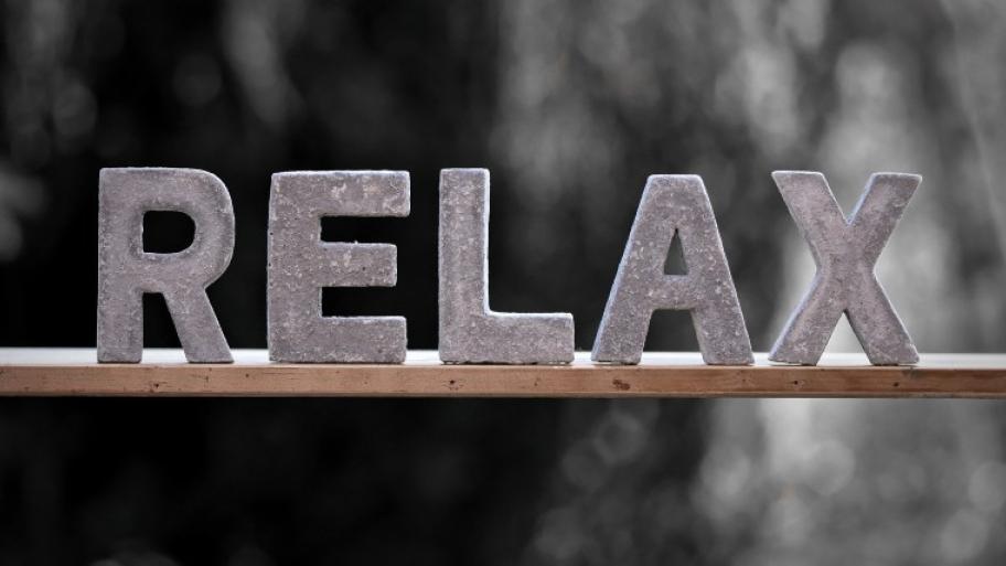 Steinbuchstaben stehen auf Holzleiste und bilden das Wort "Relax"