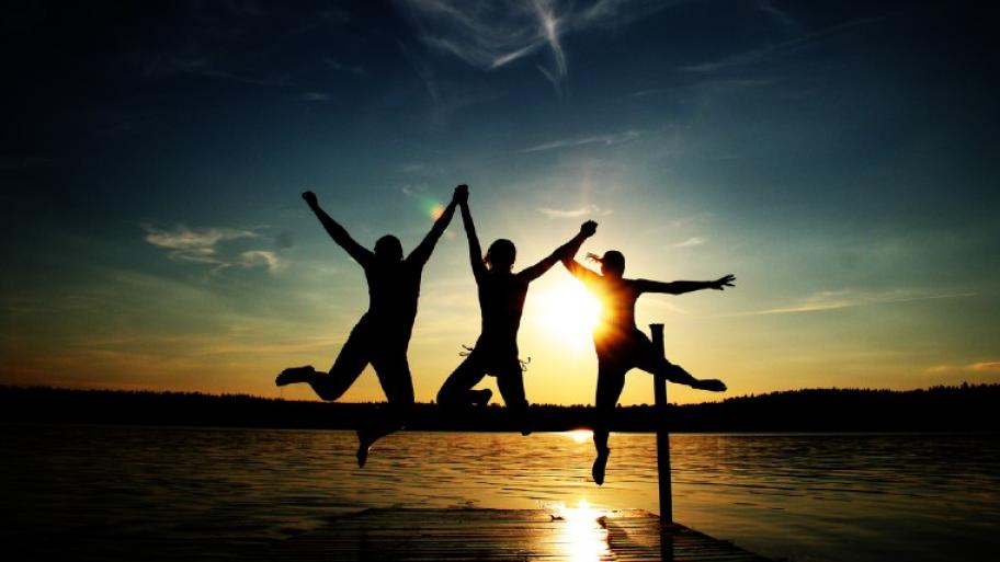 Drei Schatten: Kinder springen vom Steg aus ins Wasser am Horizont ist ein Sonnenuntergang