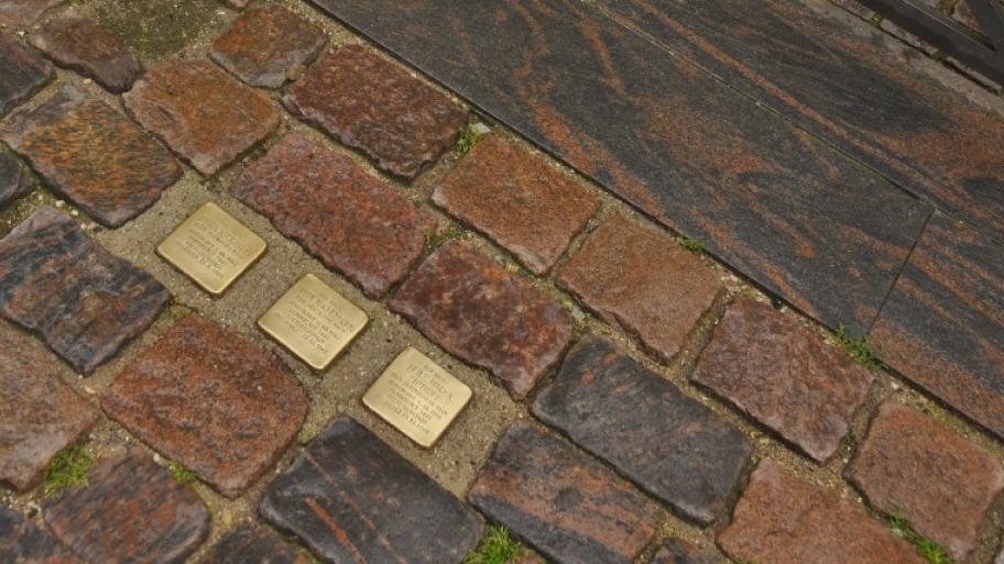 zwischen anderen Pflastersteinen 3 in den Boden eingelassene Stolpersteine aus Messing, darauf Name und Lebensdaten von Menschen, die im Nationalsozialismus umgebracht wurden