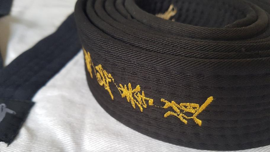Schwarzer Gurt beim Taekwondo, gelber Schriftzug, liegt aufgerollt auf einem Taekwondo Anzug