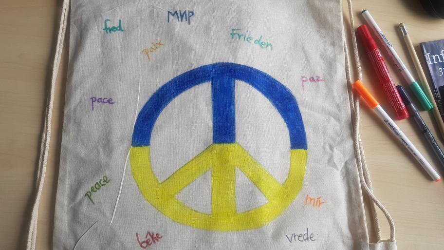 heller Beutel mit einem Peace-Zeichen in den Farben der Ukraine-Flagge mit dem Wort "Frieden" in verschiedenen Sprachen darum