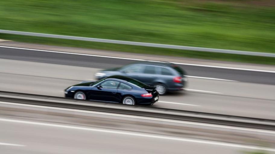 Zwei Autos auf der Autobahn, das linke Auto auf der Überholspur überholt das rechte Auto mit hoher Geschwindigkeit; Bild im Hintergrund verschwommen