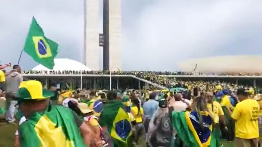 eine große Zahl Demonstrierender in gelb gekleidet und mit brasilianischen Flaggen stürmt das brasilianische Kongressgebäude in Brasilia, das im Hintergrund zu sehen ist