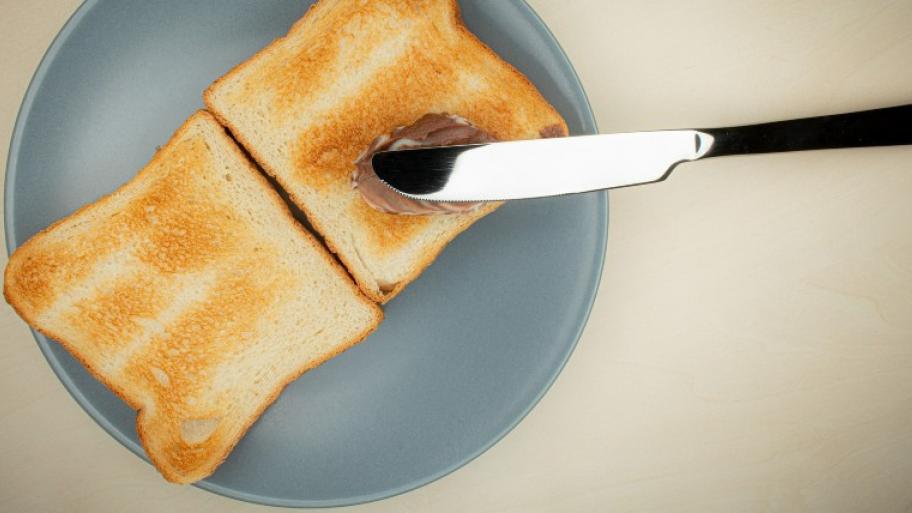 auf einem hellblauen Teller liegen zwei Toastscheiben, auf dem rechten Toast liegt ein silbernes Messer mit Schokocreme