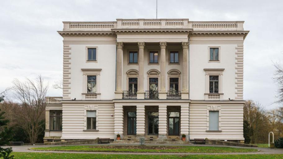 ein weißes Haus ist im Vorderegrund zu sehen. Im Hintergrund kann man ein grauen Himmel und links un rechts Bäume sehen. Unten auf dem befindet sich Gras