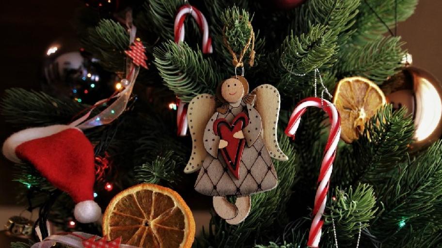 Zu sehen ist ein Holzengel, Weihnachtskugeln und Orangenscheiben, die am Weihnachtsbaum hängen.