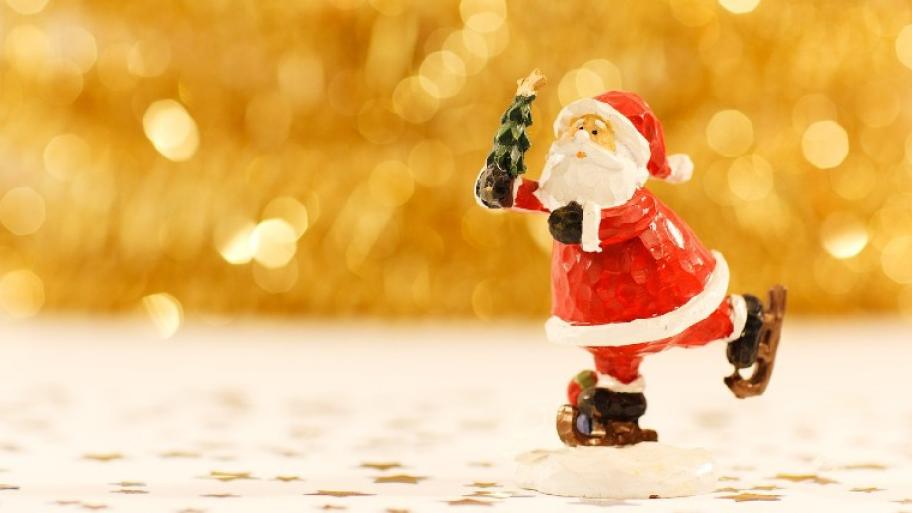 Weihnachtsmann aus Holz geschnitzt, fährt Schlittschuhe und hat einen kleinen, geschmückten Weihnachtsbaum in der Hand