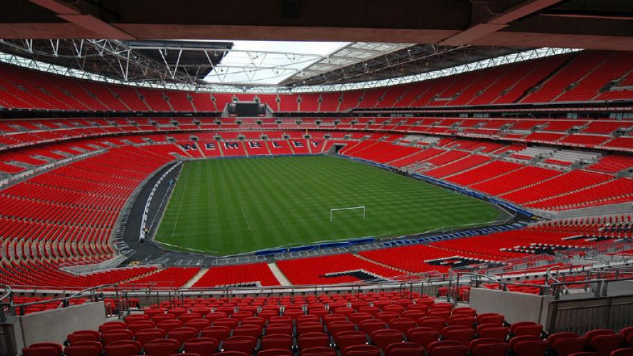 Wembley-Stadion in Deutschland. Großes ovales Stadion mit zahlreichen roten Sitzen. In der Mitte ein viereckiges grünes Feld.