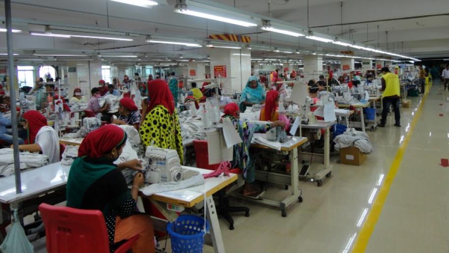 die Produktionshalle einer Textilfabrik in Bangladesch, in langen Reihen sitzen die Näherinnen an Tischen und arbeiten