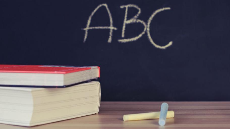 Kreide und Bücher liegen vor einer Tafel, auf der "ABC" drauf steht. 