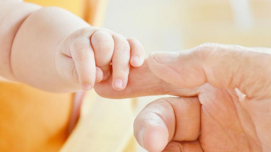 Ein Baby umklammert den Zeigefinger eines Erwachsenen. 