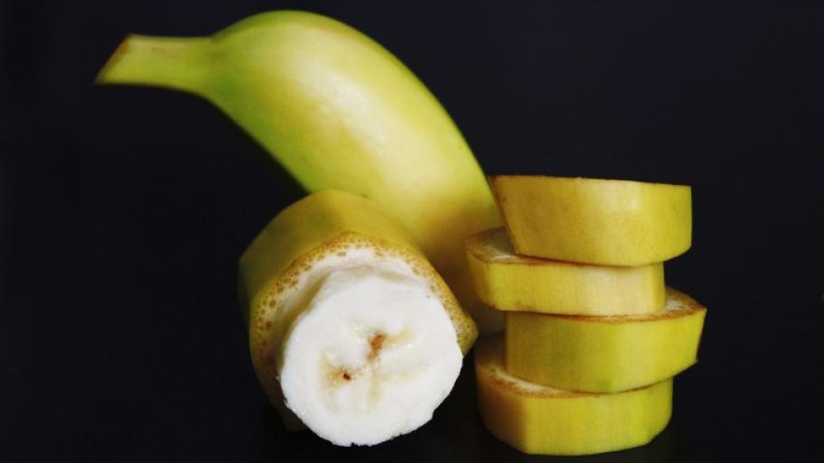 vor einem schwarzen Hintergrund steht ein Stapel Bananenscheiben mit Schale, eine halbe Banane mit Schale und eine Bananenscheibe ohne Schale
