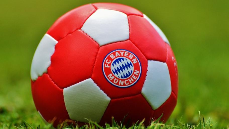 auf grünem Rasen liegt ein weiß-roter Fußball, darauf das Vereinslogo des FC Bayern München