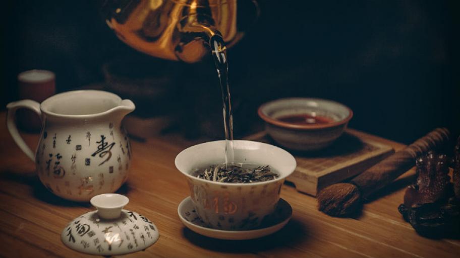 Eine Teekanne und eine Teetasse. In der Teetasse sieht man verschiedene Kräuter.