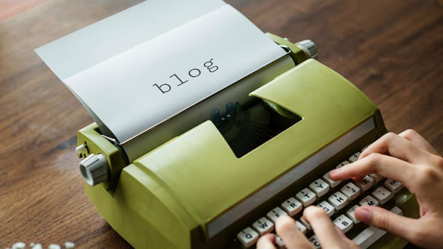 Aus einer Schreibmaschiene regt ein Blatt Papier, auf dem "Blog" geschrieben ist. 