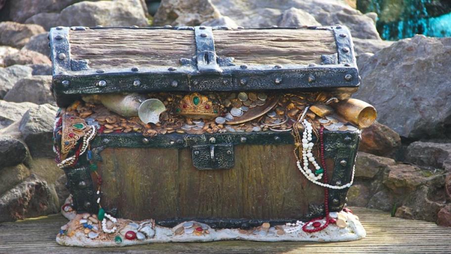 Eine alte Holztruhe gefüllt mit Ketten, Gold, Schmuck und goldenem Geschirr.