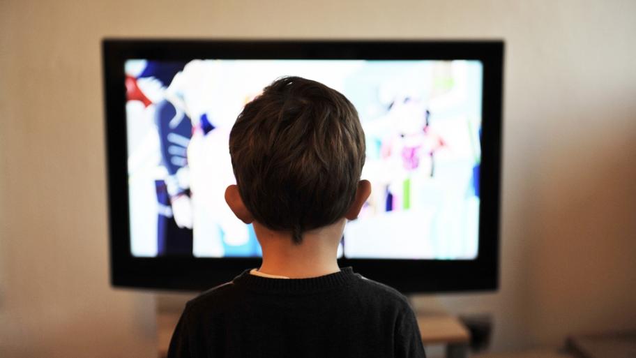 Ein Junge steht mit dem Rücken zur Kamera vor einem Fernseher. 