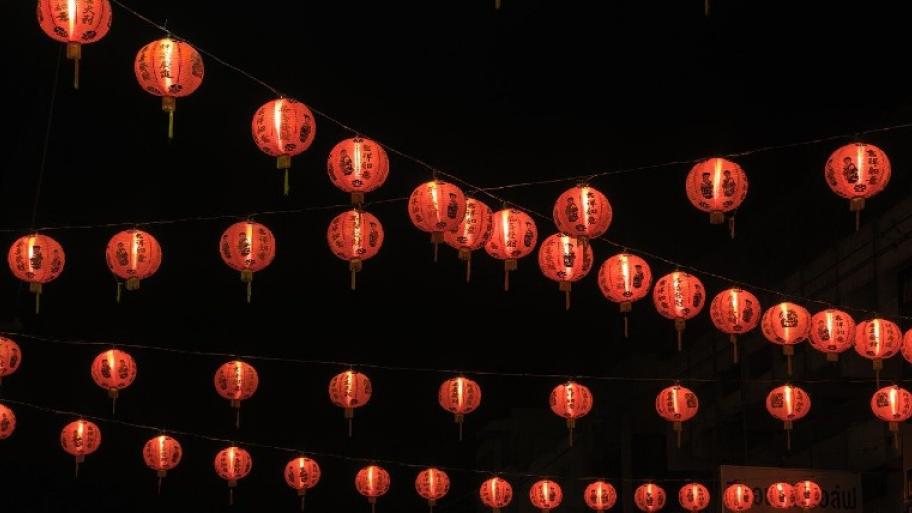 Viele rot-orangefarbenen Lampignos hängen an mehreren Seilen. Auf ihnen sind chinesische Schriftzeichen. Der Hintergrund ist schwarz.