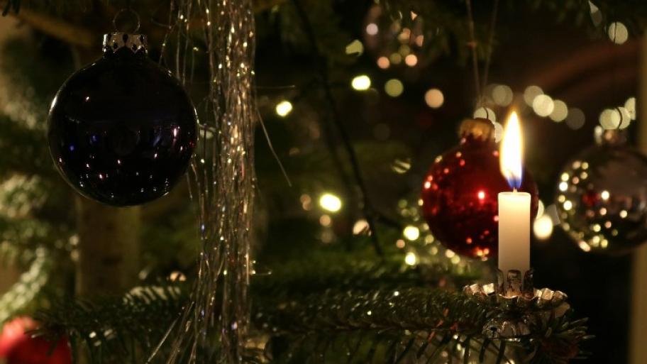 Das Bild zeigt einen geschmückten Weihnachtsbaum. Im Vordergrund sind eine Kerze und eine Weihnachtskugel zu sehen.