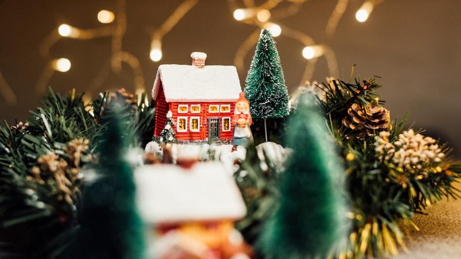 Das Bild zeigt ein rotes Miniaturhaus in einer weihnachtlichen Landschaft. Eine Elfenfigur steht davor.