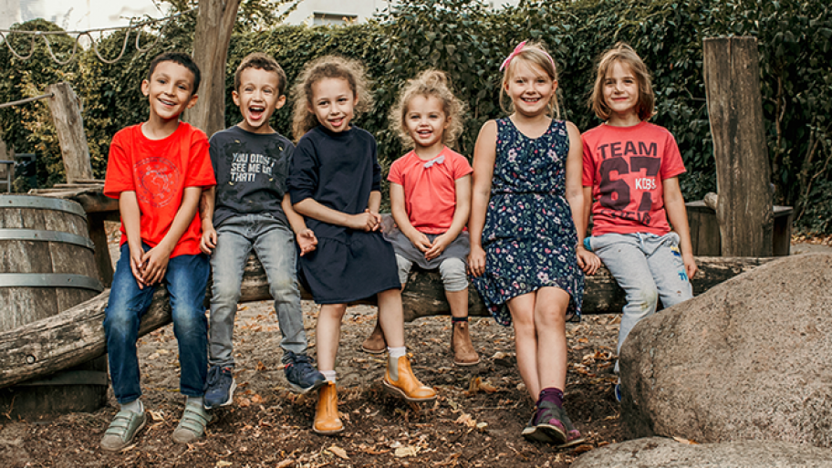 6 Fröhliche Kinder sitzen auf einem Baumstamm