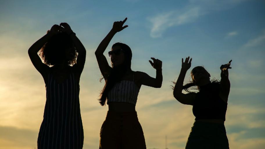 Drei Jugendliche tanzen im Sonnenuntergang und heben ihre Hände in die Luft