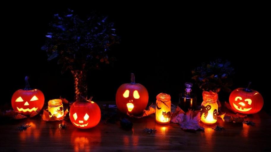 eine Reihe von ausgehöhlten Kürbissen und gläsernen Windlichtern mit Helloween Dekoration, die im Dunkeln leuchten