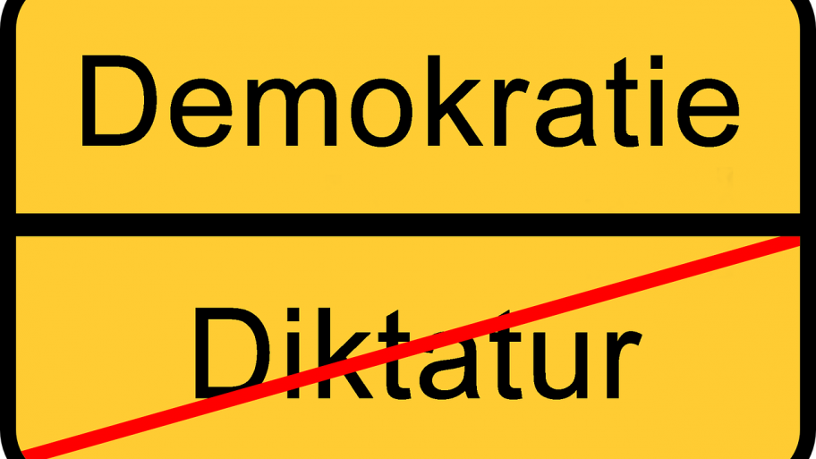 Gelbes Schild mit "Demokratie" oben, darunter ein Trennstrich und darunter das Wort "Diktatur" durchgestrichen