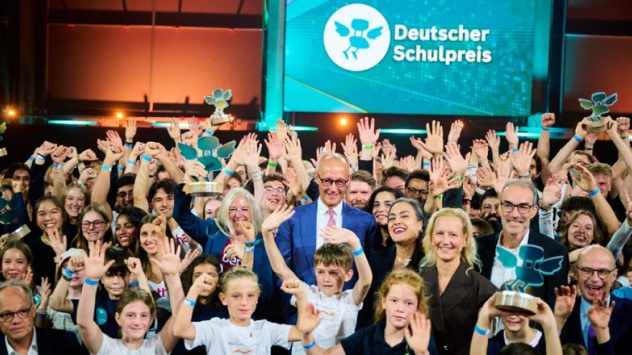 Eine große Gruppe von Kinder, Jugendlichen und Erwachsenen stehen auf der Bühne und jubeln, ein paar Kinder halten einen Preis in die Höhe