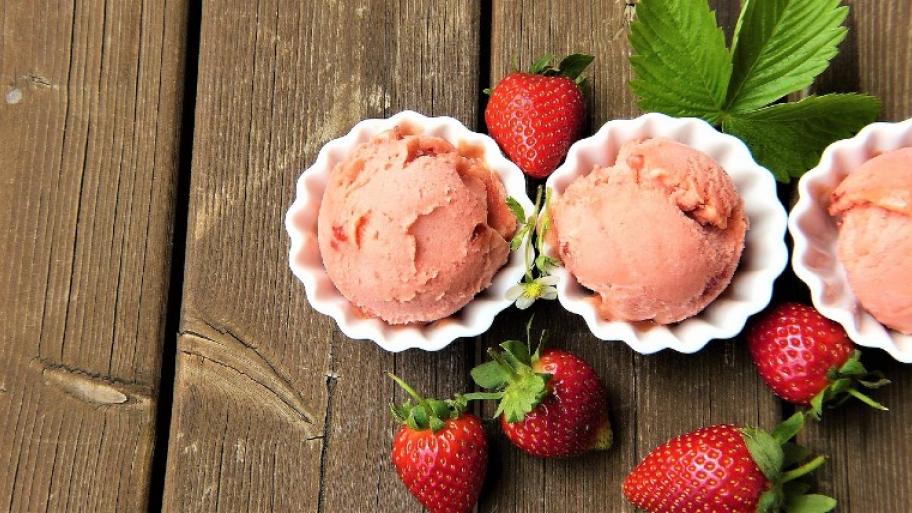 Drei rosa Kugeln Erdbeereis mit Erdbeeren im Hintergrund.