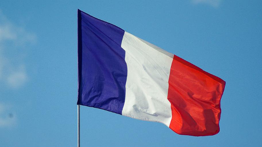 im Hintergrund hellblauer Himmel, davor weht die französische Flagge an einem Fahnenmast, von links nach rechts blau-weiß-rot längsgestreift