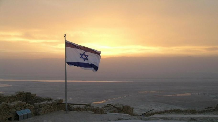Blau-weiße israelische Flagge vor Sonnenuntergang auf einem Felsen in einer Berglandschaft
