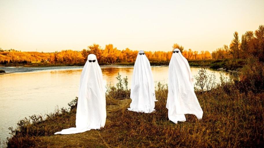 drei Menschen haben sich als Geister verkleidet. Und stehen auf einem Feld.