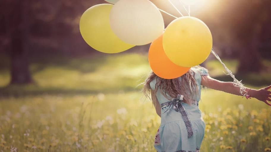 Mädchen von hinten rennt über eine Wiese mit Luftballons in der Hand
