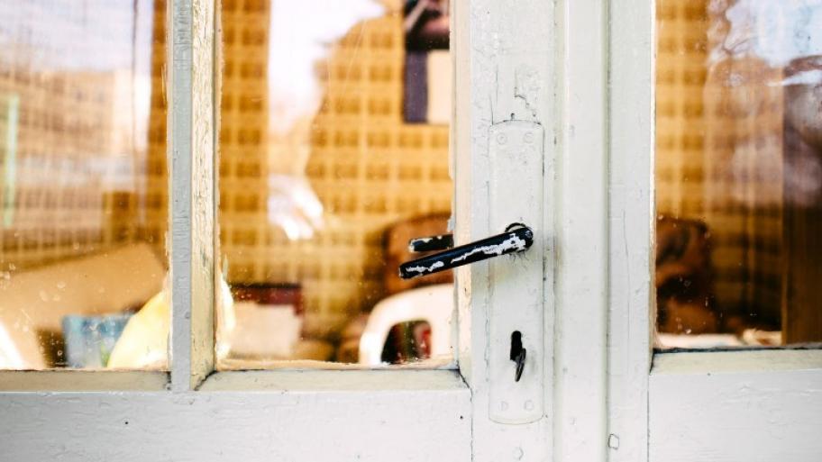 Blick durch eine geschlossene Glastür mit weißem Holzrahmen in einer dahinterliegendes Zimmer